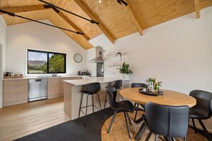 Eine moderne Küche mit Holzbalkendecke, einem großen Fenster und einem Essbereich mit rundem Tisch und Stühlen.