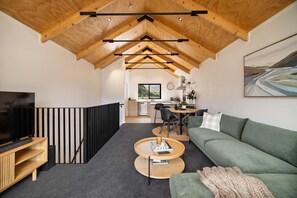 Ein modernes Interieur mit einer Loft-Decke, einem grünen Sofa, einem Couchtisch und einem Fernseher auf einem Holzboden.