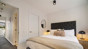 A bedroom with a large bed, a dark headboard, two bedside lamps, and a door leading to another room. - Prime Location, Walk to town, Queenstown (Queenstown)