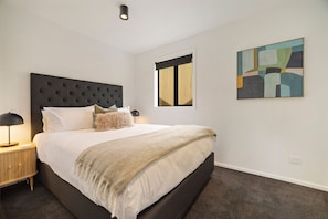 A modern bedroom with a large bed, a nightstand with a lamp, a mirror, and abstract wall art. - Prime Location, Walk to town, Queenstown (Queenstown)