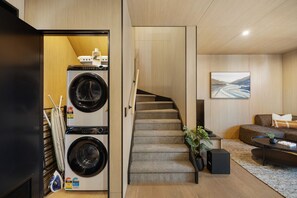 A compact living space with a washing machine, a staircase, a sofa, and a painting on the wall.