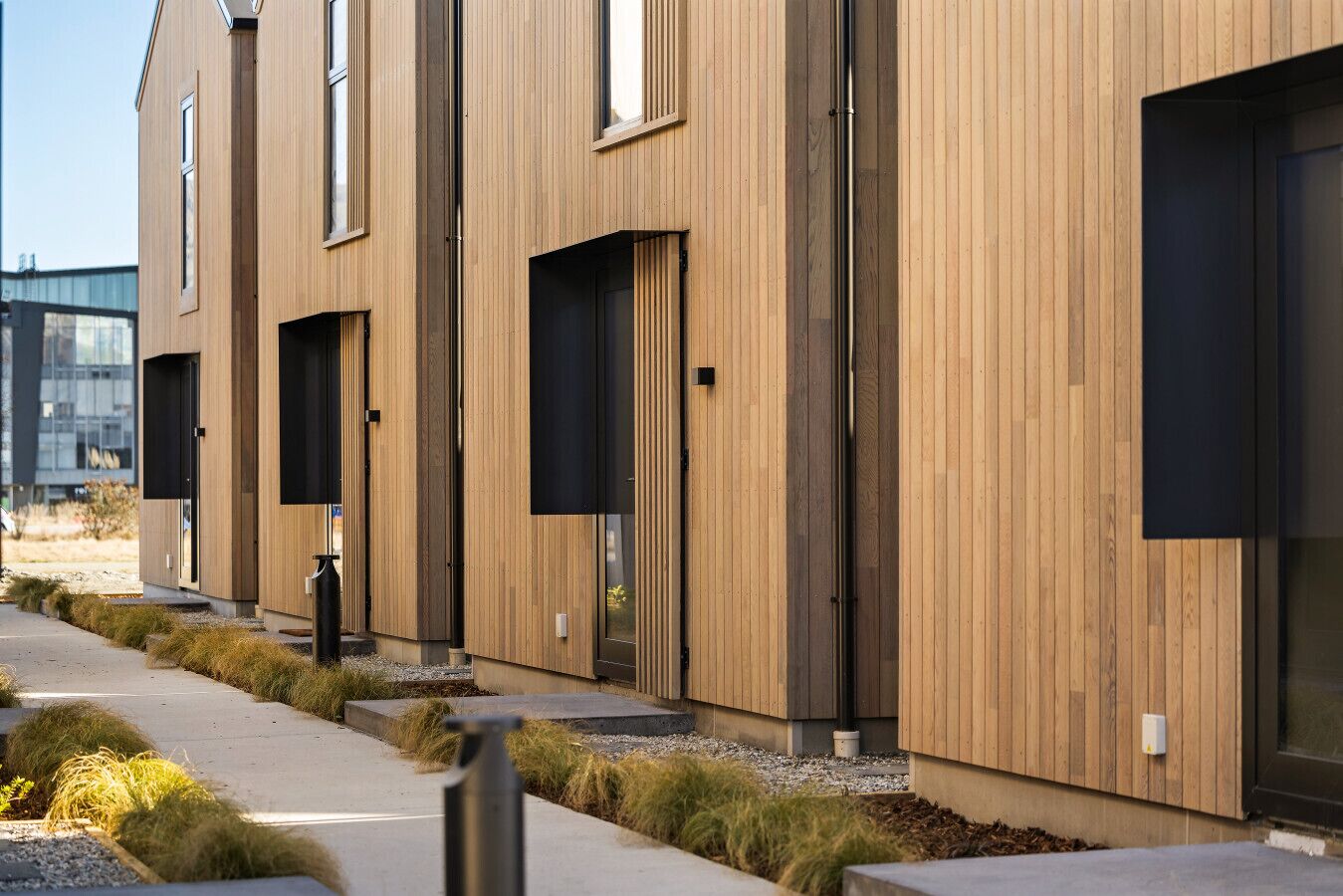 A modern building with a wooden facade, large windows, and a pathway with grass and gravel.
