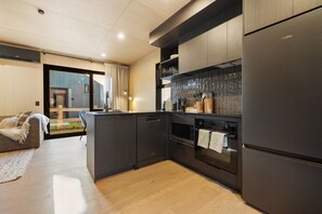 A modern kitchen with dark cabinetry, a built-in oven, and a refrigerator. - Kawarau Villa, Queenstown (Queenstown)