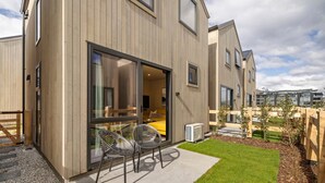 Ein modernes Gebäude mit Holzfassade, großen Schiebeglastüren und einer kleinen Terrasse mit zwei Stühlen und einem Tisch.