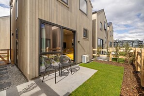 Ein modernes Gebäude mit Holzfassade, großen Schiebeglastüren und einer kleinen Terrasse mit zwei Stühlen und einem Tisch.