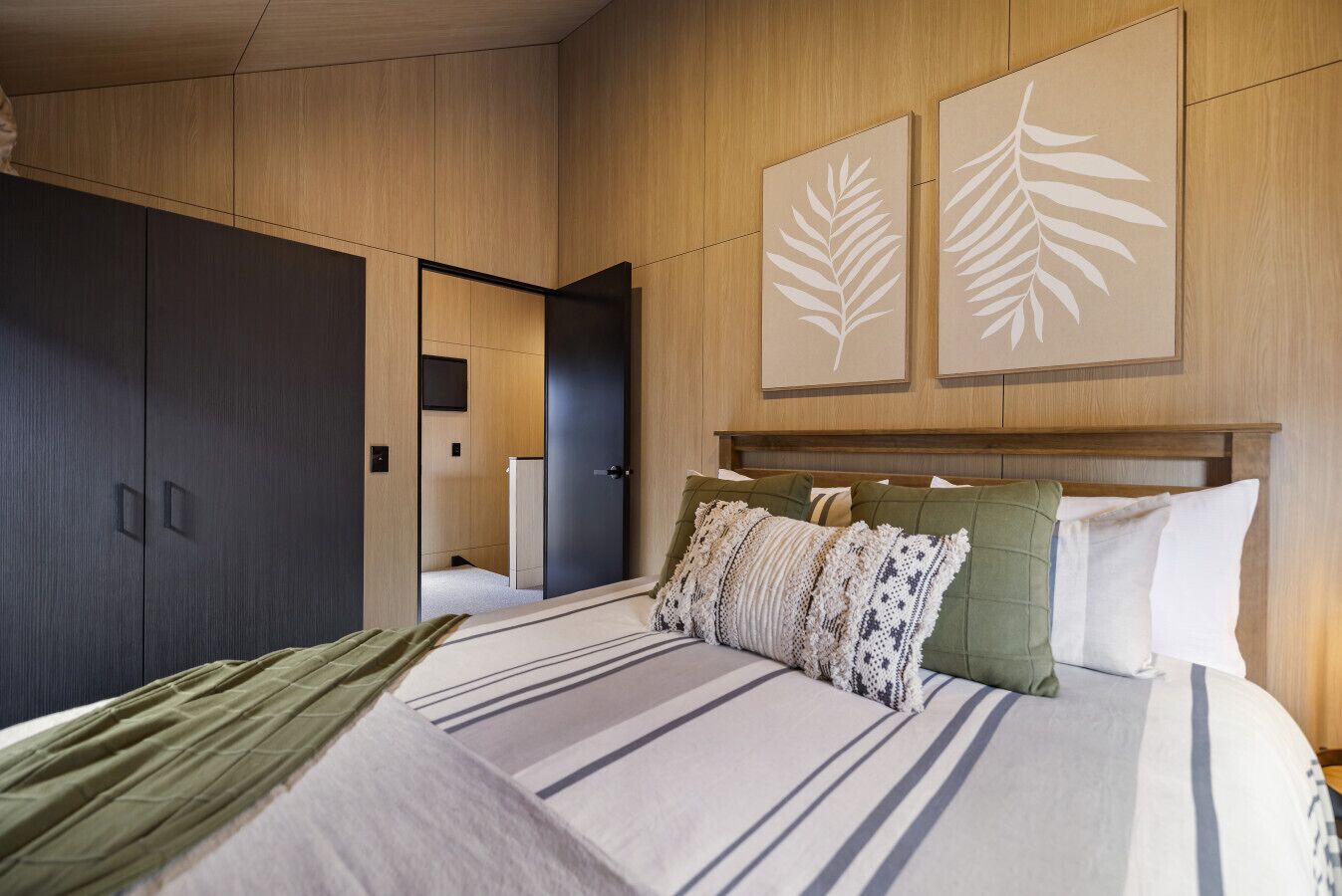 Een moderne slaapkamer met een groot bed, een donkere kast en twee kunstwerken met een bladmotief.