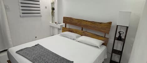 A bedroom with a bed, a ceiling fan, an air conditioning unit, a wall-mounted shelf with plants, and a bedside table with a lamp.