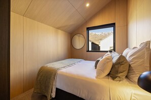 A bedroom with a bed, pillows, a bedside table, a mirror, and a window with a mountain view. - Te Awa River Retreat w Private Parking (Queenstown)