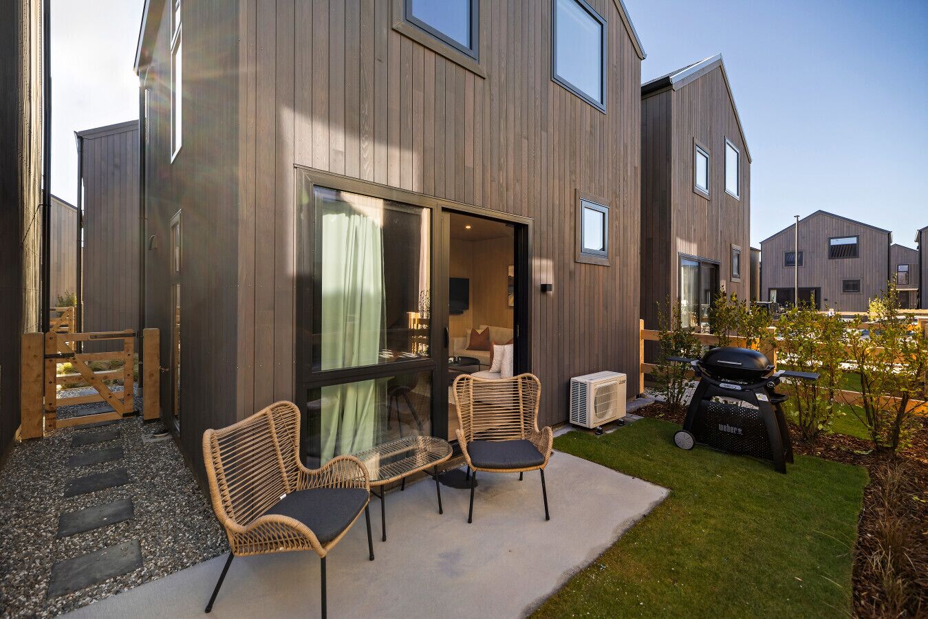 Une maison moderne dotée d’un patio aménagé avec des fauteuils en osier et un barbecue.