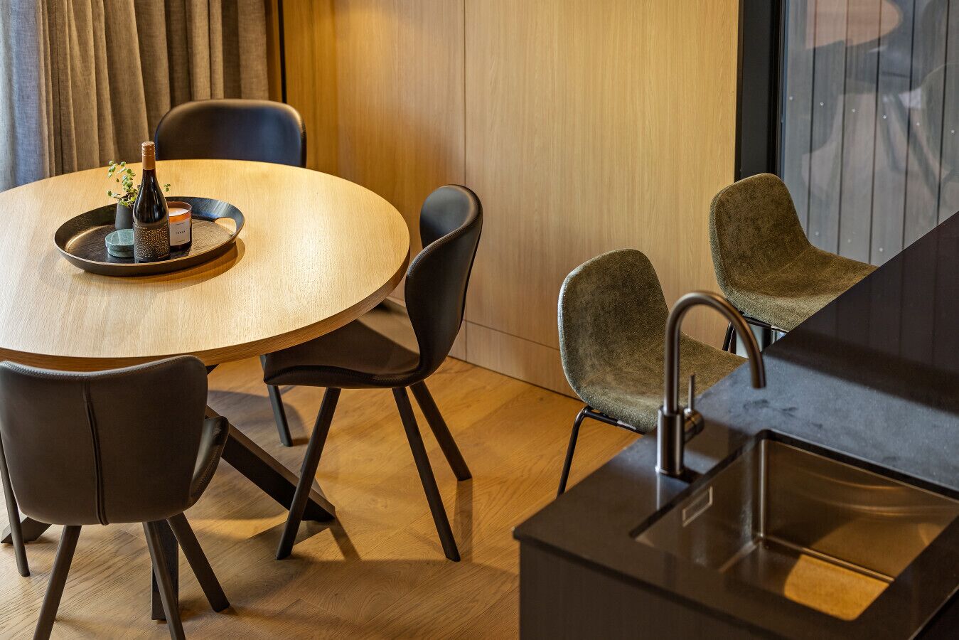 Un espace repas moderne avec une table ronde en bois, des chaises noires et une petite plante en pot.