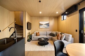 A modern interior with a staircase, a living area with a sofa, a coffee table, and a TV mounted on the wall. - Te Awa River Retreat w Private Parking (Queenstown)