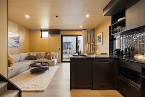 A modern kitchen with dark cabinetry, a built-in dishwasher, and a coffee maker. - Te Awa River Retreat w Private Parking (Queenstown)