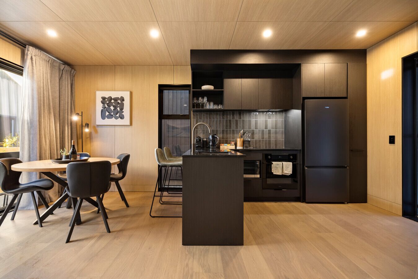A modern kitchen with a central island, dark cabinetry, and a dining area with chairs.