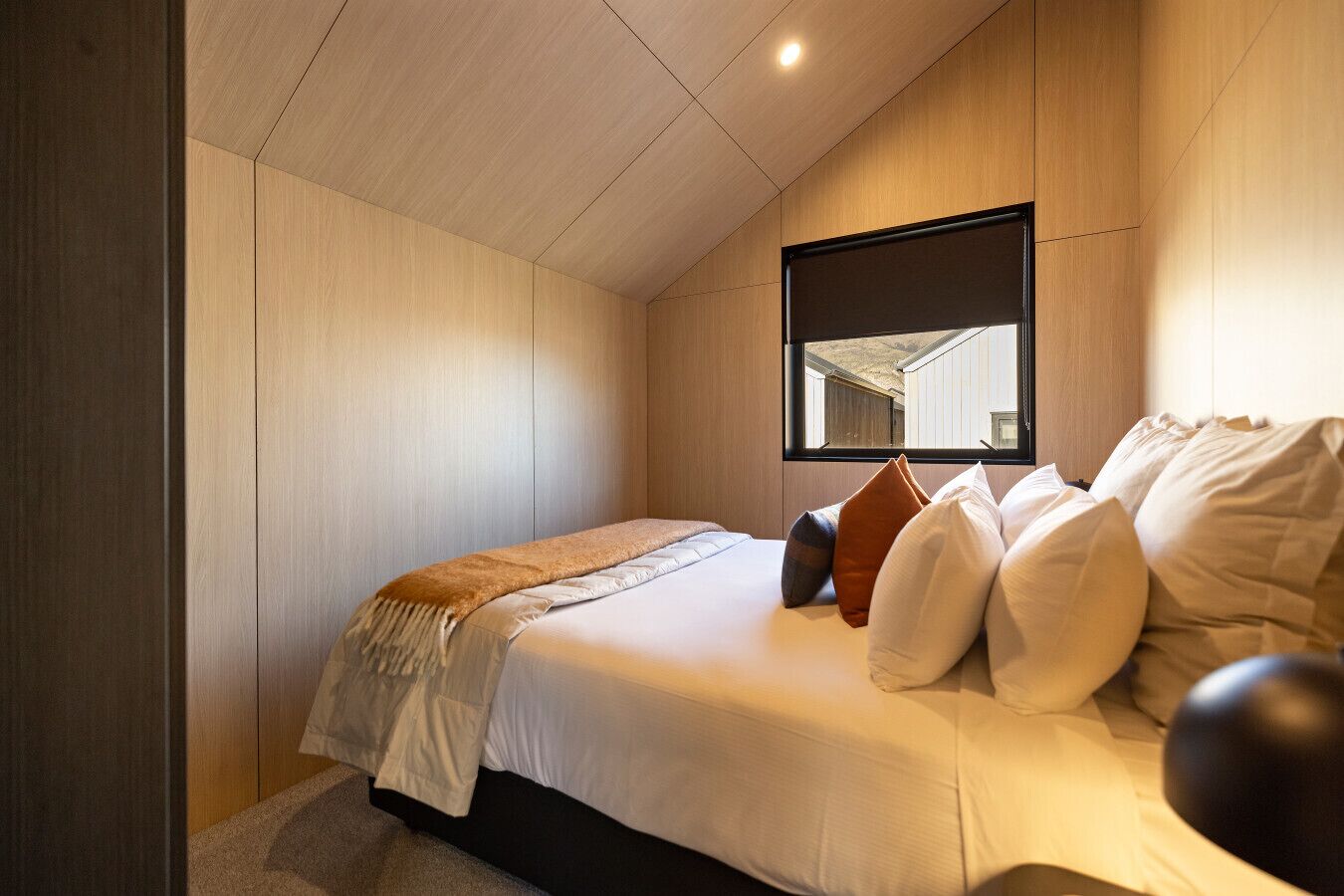 A bedroom with a bed, pillows, a blanket, a window, and wooden panel walls.