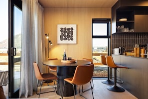 Een moderne eetruimte met een ronde tafel, vier oranje stoelen, een wijnfles en een lijst met abstracte kunst.