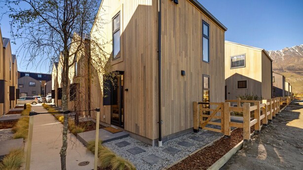 Un bâtiment moderne doté d’une façade en bois, d’une entrée sécurisée par un portail et d’un chemin de gravier menant à la porte.