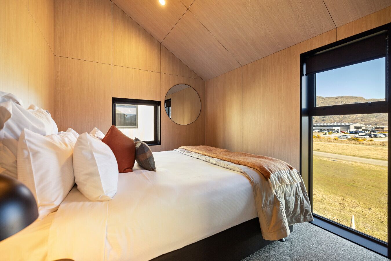 Een moderne slaapkamer met een groot bed, een ronde spiegel en uitzicht op een woestijnlandschap door een groot raam.