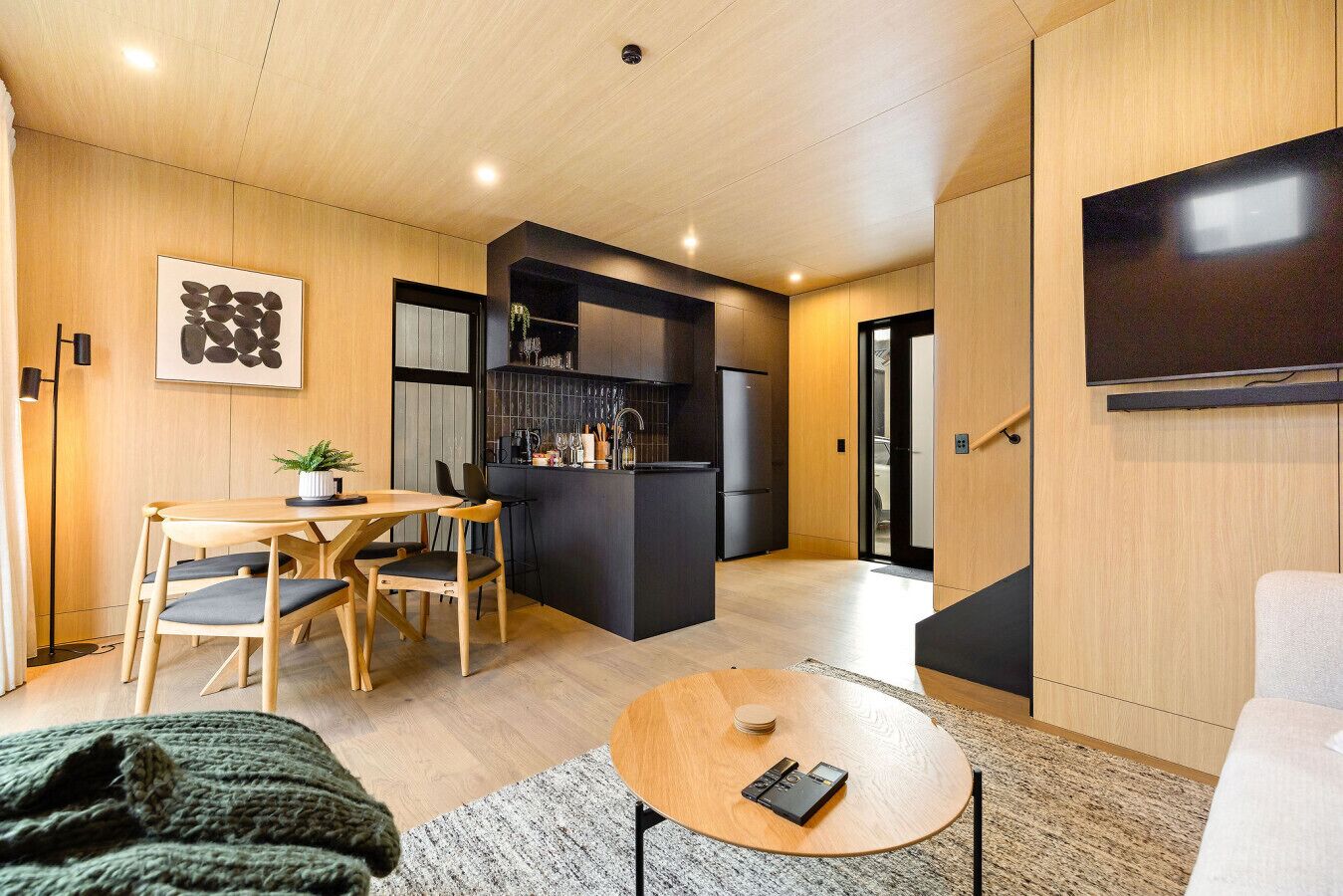 Un espacio habitable compacto con zona de comedor, kitchenette y televisor de pantalla plana montado en la pared.