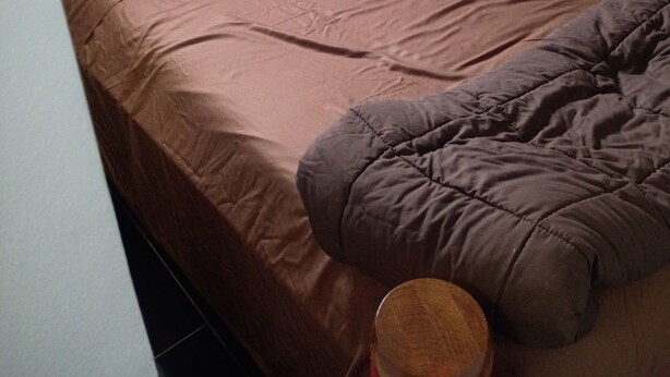 Uma cama com colchão marrom, cabeceira vermelha e travesseiro marrom.