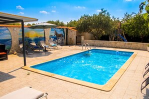 Ein rechteckiger Pool mit einer gefliesten Liegefläche, umgeben von Liegestühlen und einem Wandgemälde.