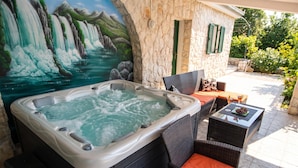 Een jacuzzi met een watervalreliëf, buitenzitplaatsen en een stenen muur.