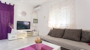 Een moderne woonkamer met een flatscreen televisie, een bank, een salontafel en een potplant.