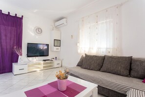 Ein modernes Wohnzimmer mit Flachbildfernseher, einer Couch, einem Couchtisch und einer Topfpflanze.