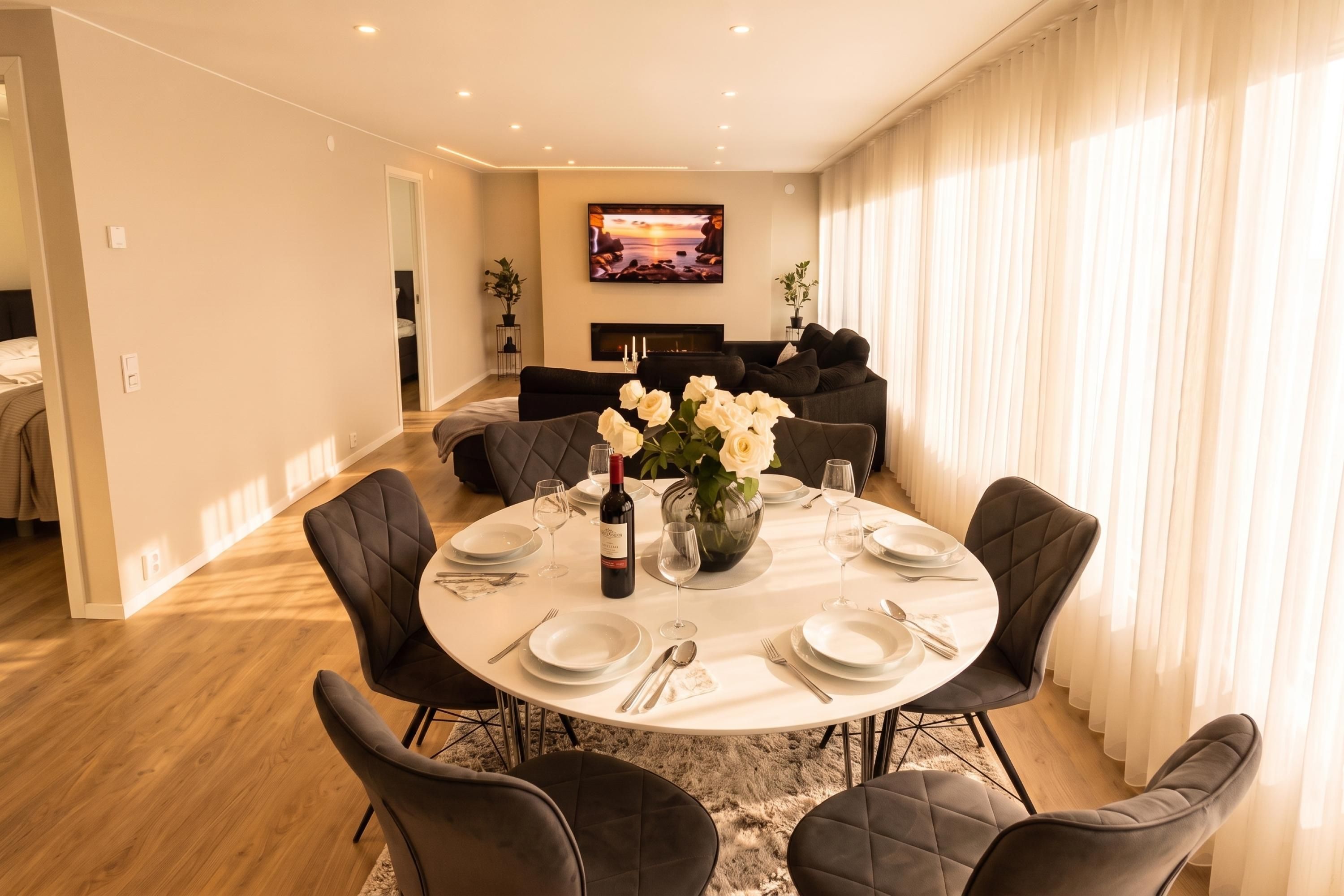 A dining area with a round table set for six, surrounded by dark upholstered chairs.