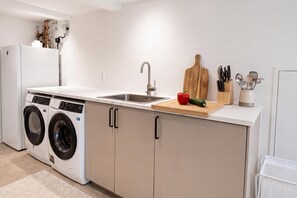 Een kleine keuken met een wasmachine, een spoelbak en een snijplank met groenten.