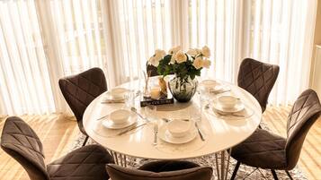Une table de salle à manger ronde, dressée pour six personnes, avec de l’argenterie, des assiettes blanches et un vase rempli de fleurs blanches.