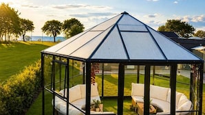 Un belvédère avec un toit de verre, doté de mobilier blanc et offrant une vue sur la mer.