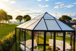 A glass-roofed gazebo with white furniture and a view of the sea.