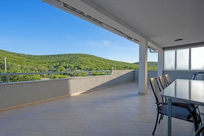 Ein Balkon mit Tisch und Stühlen, Blick auf grüne Hügel und einen klaren Himmel.