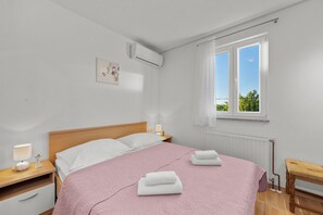 Ein Schlafzimmer mit einem Bett, Nachttischen, einem Fenster und einer Klimaanlage.