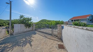 A paved entrance with a metal gate, a concrete wall, and a house with a red roof in the background. - Pool Villa Marija, Šibenik, Croatia (Šibenik)