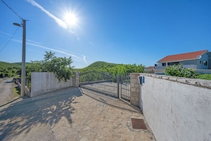 Ein gepflasterter Eingangsbereich mit einem Metallgitter, einer Betonmauer und einem Haus mit rotem Dach im Hintergrund.