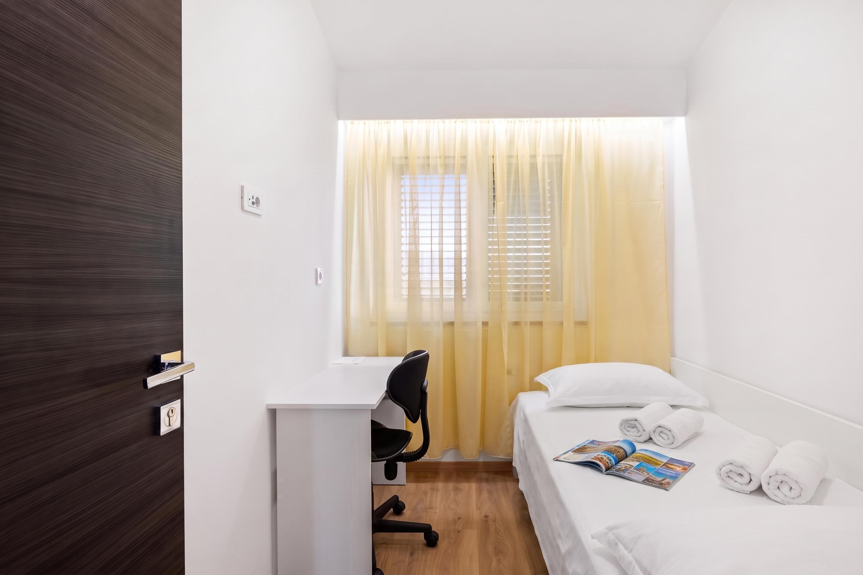 Ein kleines, ordentlich eingerichtetes Hotelzimmer mit Bett, Schreibtisch und Stuhl.