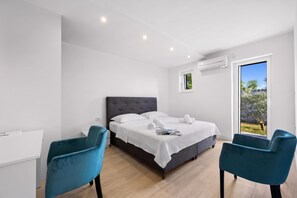 Ein modernes Schlafzimmer mit einem Bett, zwei Stühlen, einem Schreibtisch und einem großen Fenster.