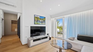 A modern living room with a flat-screen TV, a glass coffee table, a sofa, and a sliding glass door leading to an outdoor area. - Holiday Home Eros with Pool, Šibenik, Croatia (Šibenik)