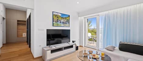 A modern living room with a flat-screen TV, a glass coffee table, and a sofa.