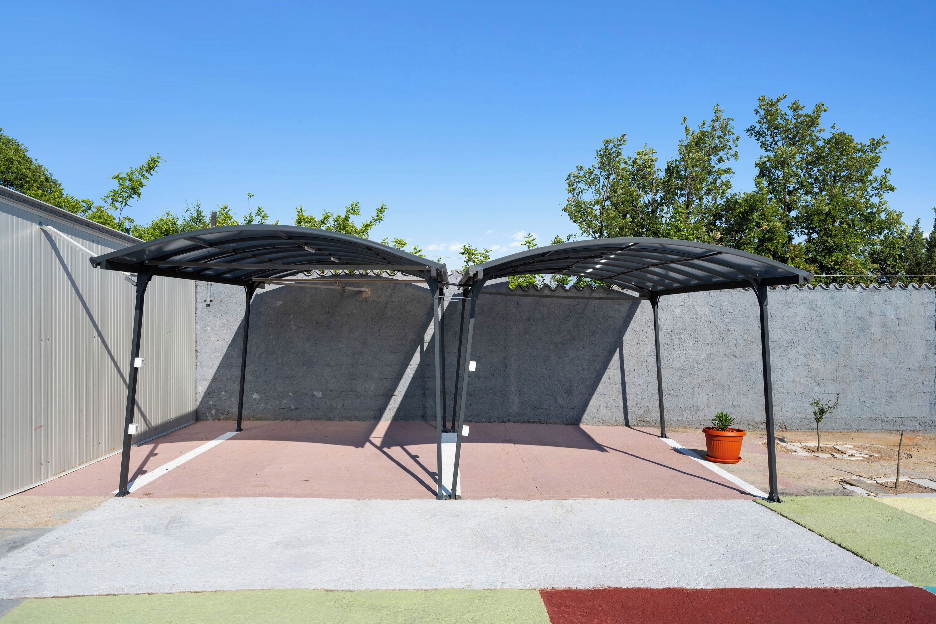 A covered outdoor area with a metal frame, a concrete wall, and a potted plant.