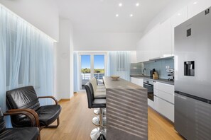 A modern kitchen with a stainless steel refrigerator, a dining area with a long table and chairs, and a view through a glass door. - Holiday Home Eros with Pool, Šibenik, Croatia (Šibenik)