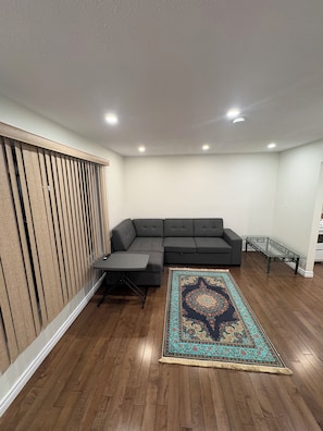 A living room with a sectional sofa, a glass coffee table, a patterned rug, and wooden flooring. - Modern Ottawa Suite | Private Entrance & Free Parking (Ottawa)