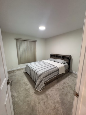 A bedroom with a bed, a window with blinds, and a carpeted floor. - Modern Ottawa Suite | Private Entrance & Free Parking (Ottawa)