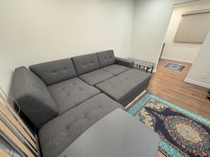 Un sofá seccional gris en una sala de estar con un rugado y una mesita con superficie de vidrio.