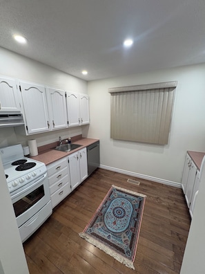 A compact kitchen with white cabinets, a stove, and a sink. - Modern Ottawa Suite | Private Entrance & Free Parking (Ottawa)