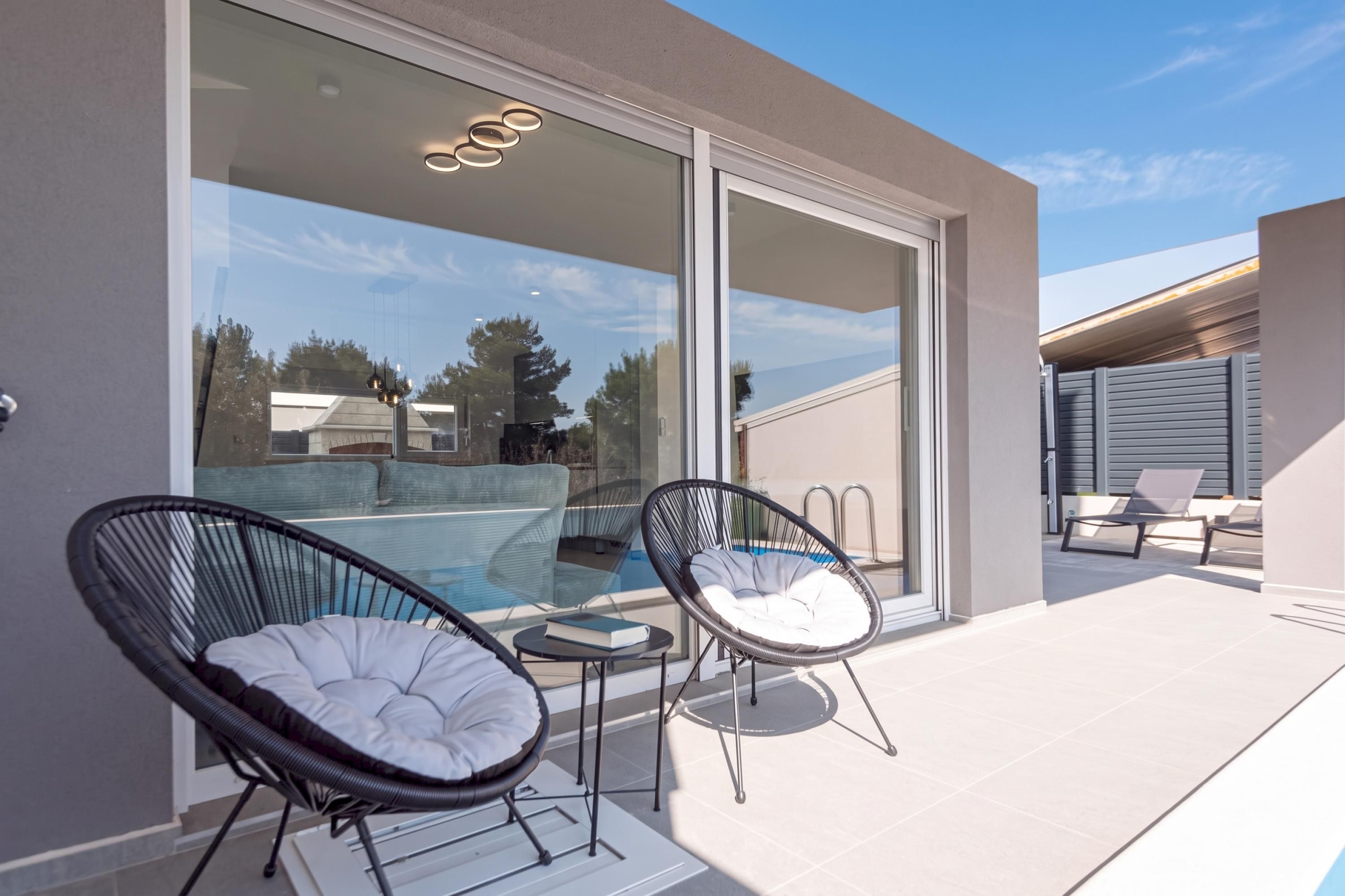 A modern outdoor area with a glass door leading to a pool, two wicker chairs, and a small table.