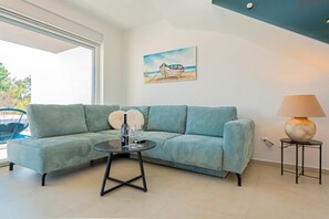 A modern living room with a green sofa, a small round table with a wine bottle and glasses, a lamp, and a painting of a boat on the wall. - Pool Villa Pomalo, Vodice, Croatia (Vodice)
