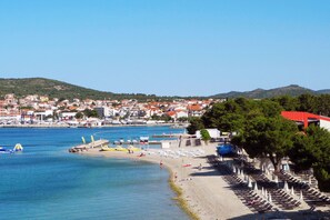 A coastal town with a beach, rows of beach umbrellas, and a clear view of the sea and distant hills. - Pool Villa Pomalo, Vodice, Croatia (Vodice)