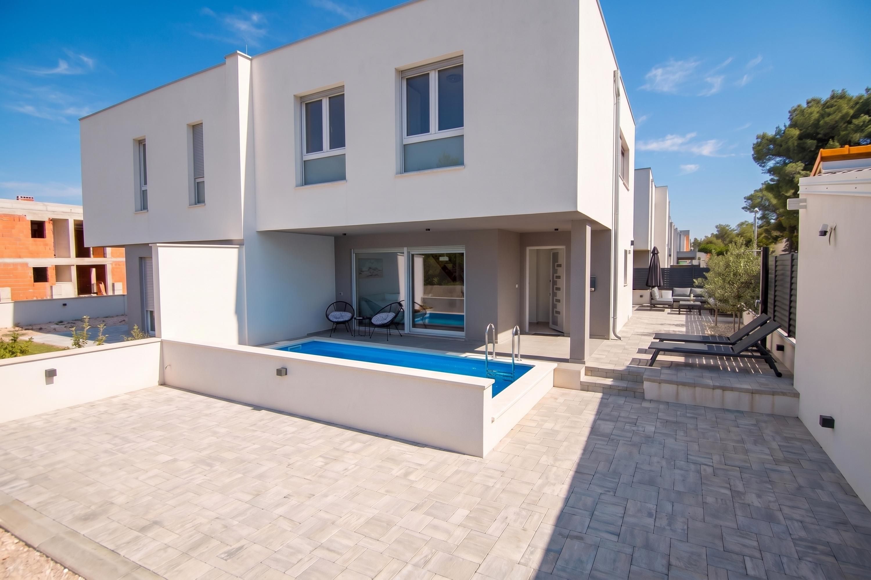 Una casa moderna de dos pisos con piscina, mobiliario exterior y cielo despejado.